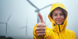 Young woman with thumb up standing in front of a wind power plant