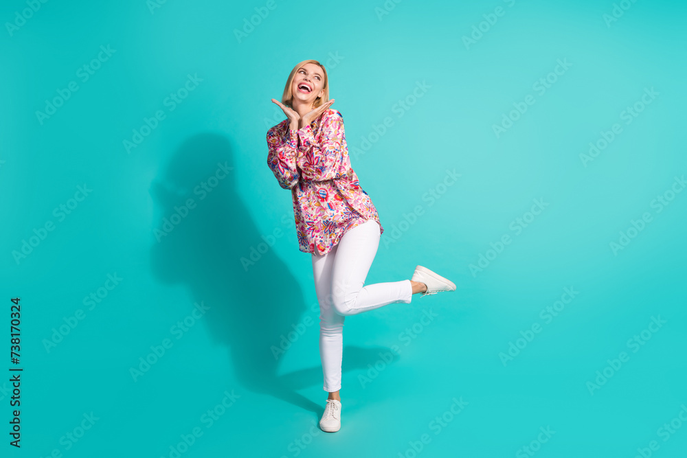 Full length photo of girlish positive woman dressed print blouse white pants look at promo empty space isolated on teal color background