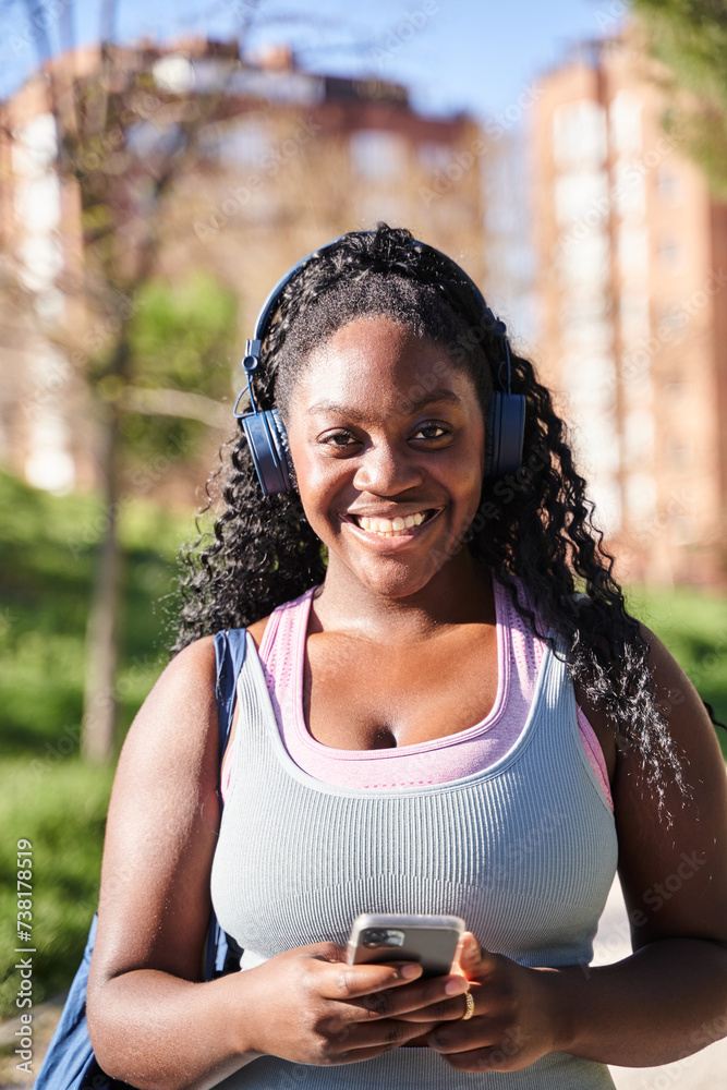 vertical portrait of a young African-American woman listening to music with headphones while holding a smartphone and looking at the camera. vertical portrait of a young African-American woman listening to music with headphones while holding a smartphone and looking at the camera.