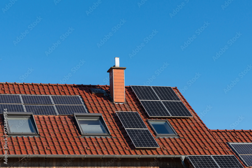 Tiled roof of a house with a chimney and solar panels under a blue sky. Tiled roof of a house with a chimney and solar panels under a blue sky.
