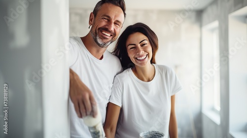 Young family couple doing renovations at home. Happy man and woman painting walls and decorating their house. Husband and wife with bucket and roller standing by wall and discussing interior design photo