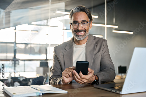 Wallpaper Mural Happy mature 45 years old business man executive sitting at desk using mobile phone. Smiling middle aged businessman looking at camera working on computer technology holding smartphone. Portrait. Torontodigital.ca