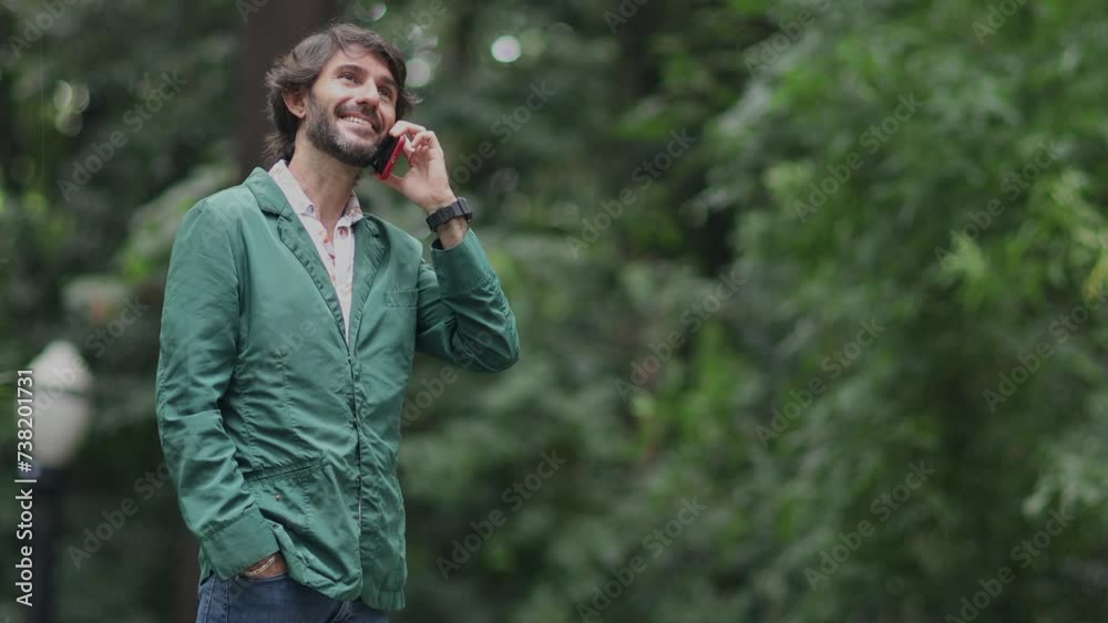 View of a young man with smartphone at daytime in a green park in the city. High quality video. View of a young man with smartphone at daytime in a green park in the city. High quality video.