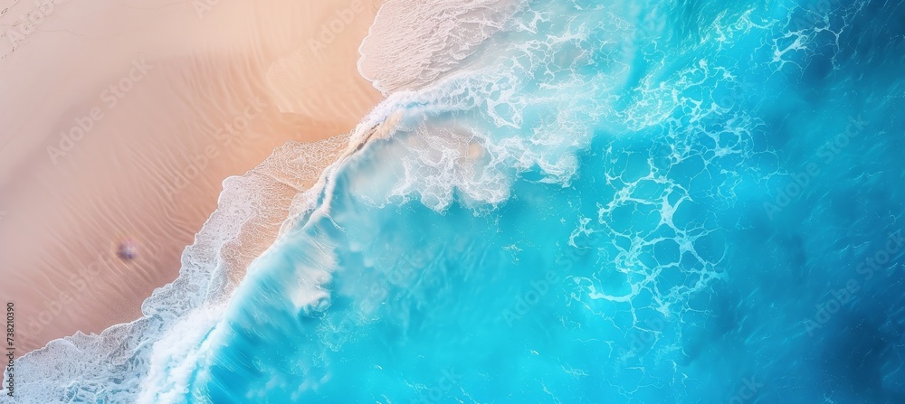 Aerial view of coastal seascape with blue ocean waves, white foam, and yellow sand beach from above.