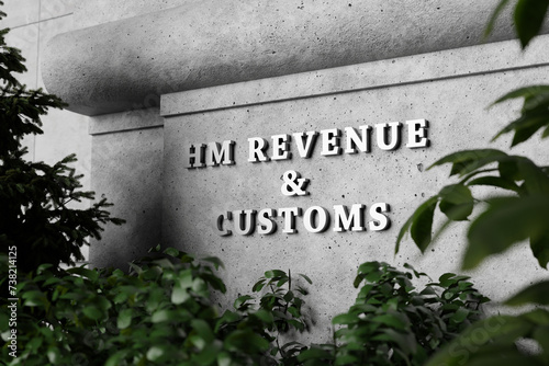 Silver sign of Home Office Revenue and Customs on a concrete wall with green plants as foreground. Illustration of the concept of taxation photo