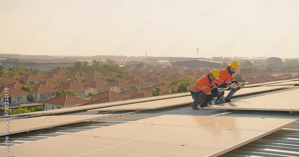 Two engineers solar technicians in reflective gear discussing working examine solar installations on rooftop panels at dusk, with suburban backdrop Two engineers solar technicians in reflective gear discussing working examine solar installations on rooftop panels at dusk, with suburban backdrop