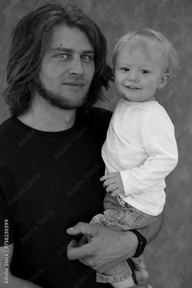 A young long-haired father holds his little son in his arms A young long-haired father holds his little son in his arms