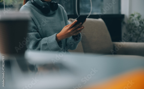 Happy pretty millennial Indian girl relaxing at home, resting in armchair, typing on smartphone, using online app, software, shopping on Internet, making video call. Mobile phone communication