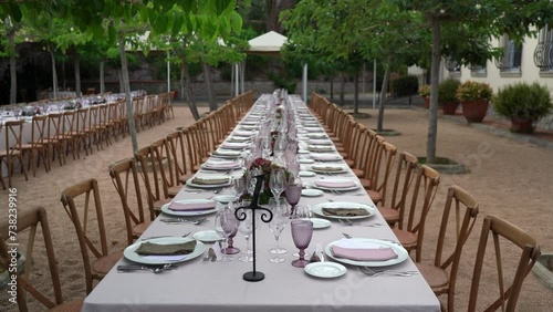 imagen estática de mesa alargada decorada, sillas de madera y arboles de fondo