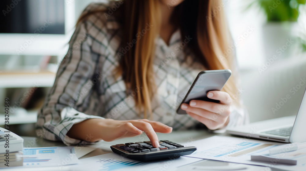 Fototapeta premium An economical woman diligently works on her phone calculator at home, efficiently managing bills and taxes online. She focused on financial planning, calculates expenditures and planning the budget