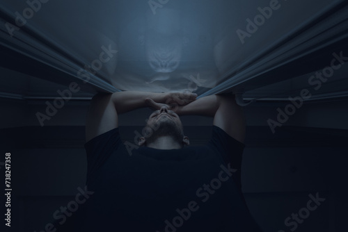 The man leans against the glass window and looks thoughtfully at the street at night. He can't sleep. Bottom angle.