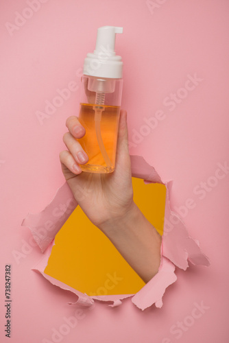 A woman's hand shows a bottle of cleansing foam through a hole in a paper background.