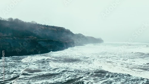 Stormy winter scene. Rough seas of the English coast with mist and fog. Aerial footage of the sleepy coastal town of Sandsend beach on the coast of north Yorkshire in England photo