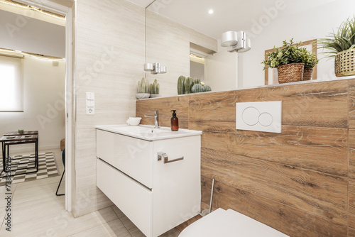 Fotografie A bathroom with wood-like stoneware tiles, white wooden furniture, endless mirro