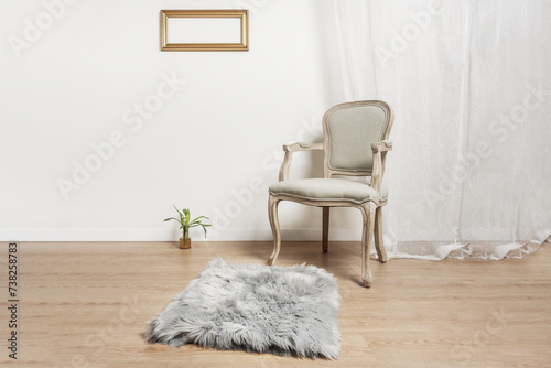 an unvarnished light wooden armchair with a gray upholstered seat, a gray rug in a room with white walls and light parquet floors, a small plant on the floor and a frame without photos on the wall photo