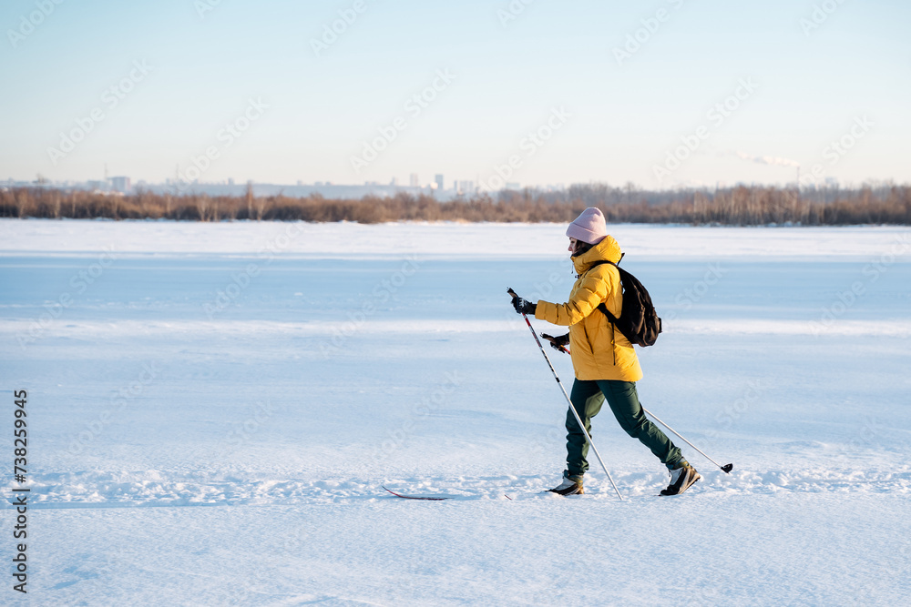 Woman on skis running on a snowy field, a lady with a backpack training in a winter forest.