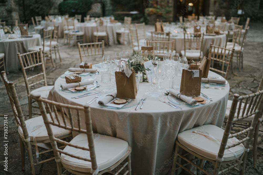 Banquete de bodas en el exterior del castillo. Mesas decoradas con manteles blancos, sillas blancas, cristalería transparente. Entorno natural, vegetación y piedra.