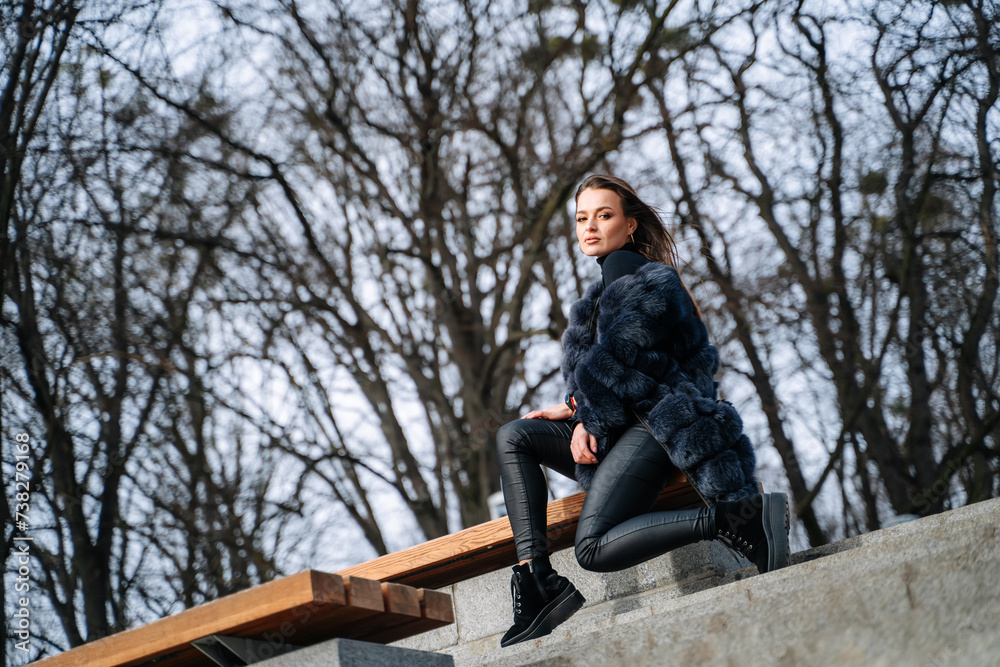 Fototapeta premium Young beautiful girl in blue coat sits on the steps in the park