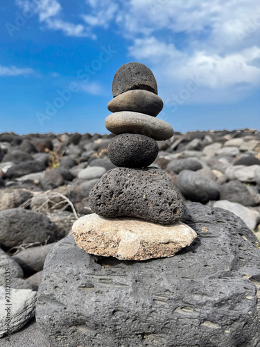 A zen-like stone pyramid structure sits on a rugged volcanic shore under blue sky with clouds, meditation, spiritual journey, connection with nature, rugged and wild