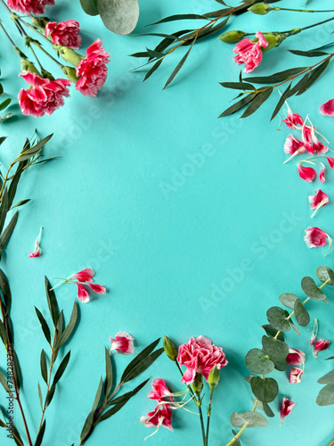 Fototapeta Naklejka Na Ścianę i Meble -  A photo featuring a blue background adorned with vibrant pink carnation flowers and lush green leaves, showcasing the natural beauty of this colorful composition. Copy-space on greeting card.