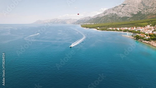 Clear blue seascape with speedboats creating white trails on water surface. Skydiving adventure seen above serene coastal town Makarska in Croatia. Summer vacations. photo