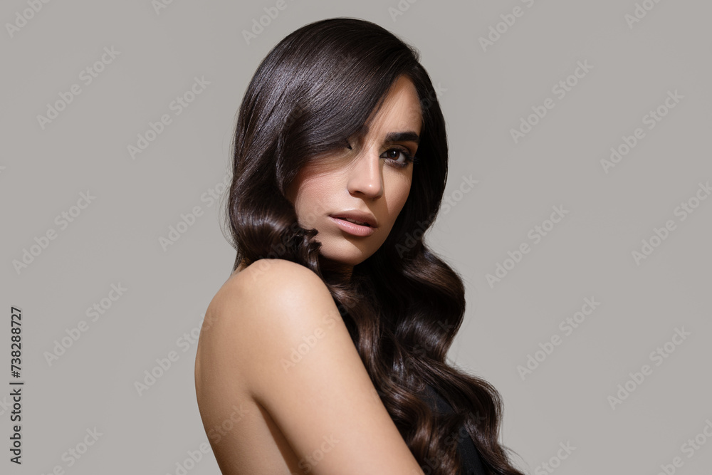 Naklejka premium Portrait of a brunette girl with luxurious wavy hair. Gray background.