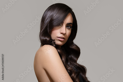 Portrait of a brunette girl with luxurious wavy hair. Gray background.