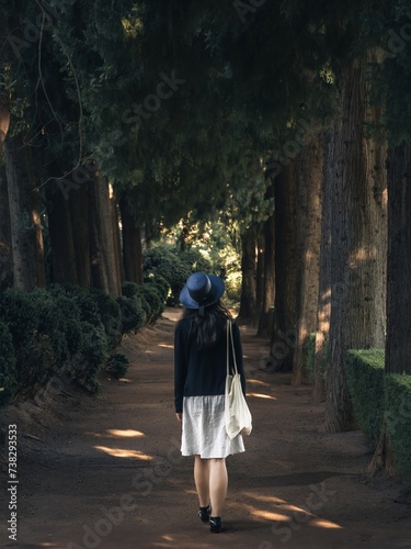A beautiful young woman from the back in a summer dress and hat walking through the Alhambra Generalife gardens