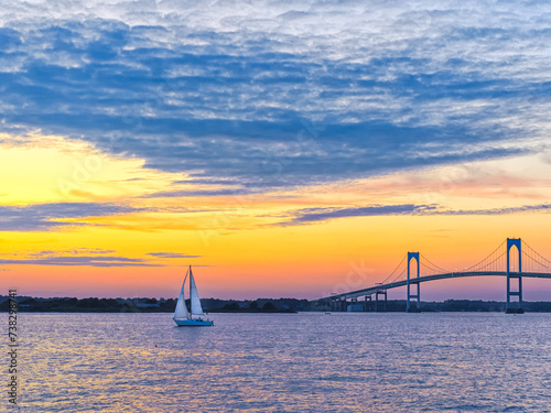 Dramatic beautiful sunset with Claiborne Pell Newport Bridge sailboat and clouds Newport, Rhode Island, USA, a popular New England holiday vacation destination in summer and fall.  photo