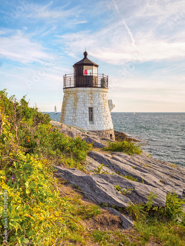 A vertical scenic view of Castle Hill Lighthouse, Newport, Rhode Island and the rocky cliffs along Narragansett Bay in the summer.