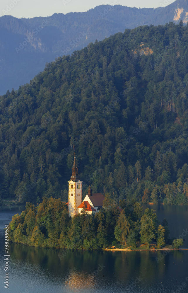 close up view of tiny island with church tower and nature in the middle of gorgeous clear water blue lake