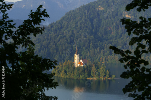 close up view of tiny island with church tower and nature in the middle of gorgeous clear water blue lake photo