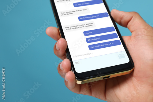 Fototapeta Naklejka Na Ścianę i Meble -  Man texting with friend using messaging application on smartphone against light blue background, closeup
