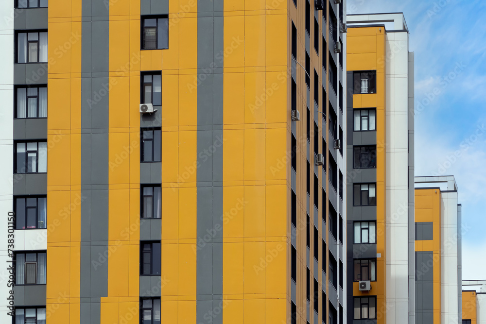 Fragment of urban block against backdrop of blue sky. Yellow and gray panels of ventilated facade on walls of buildings. Perfect for illustrating urban architecture, cityscapes, and modern design Fragment of urban block against backdrop of blue sky. Yellow and gray panels of ventilated facade on walls of buildings. Perfect for illustrating urban architecture, cityscapes, and modern design