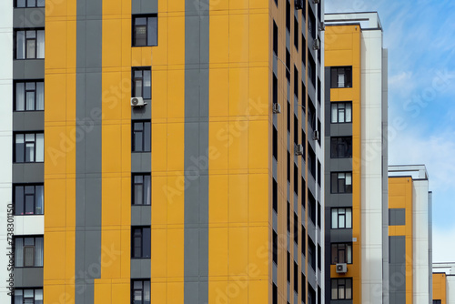 Fragment of urban block against backdrop of blue sky. Yellow and gray panels of ventilated facade on walls of buildings. Perfect for illustrating urban architecture, cityscapes, and modern design