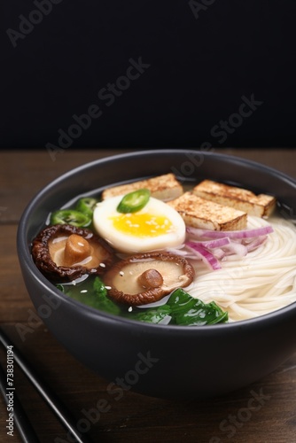 Delicious vegetarian ramen in bowl on wooden table against black background