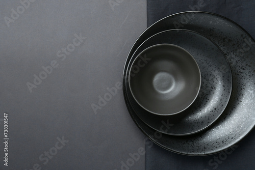Stylish ceramic plates, bowl and napkin on grey background, top view. Space for text