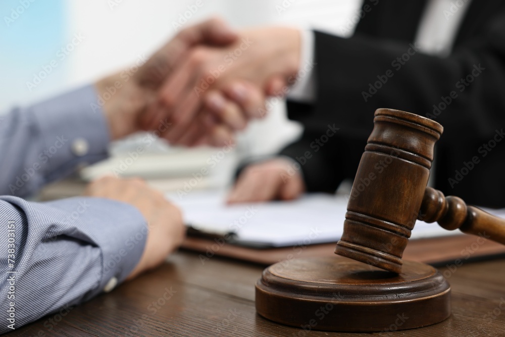 Lawyer shaking hands with client in office, focus on gavel Lawyer shaking hands with client in office, focus on gavel