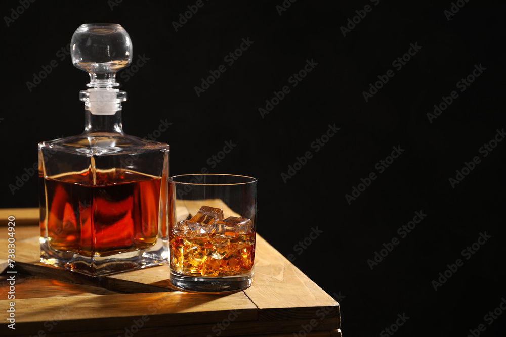 Whiskey with ice cubes in glass and bottle on wooden crate against black background, space for text Whiskey with ice cubes in glass and bottle on wooden crate against black background, space for text
