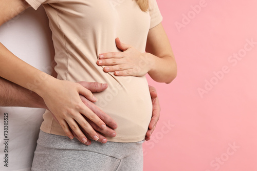 Man touching his pregnant wife's belly on pink background, closeup. Space for text