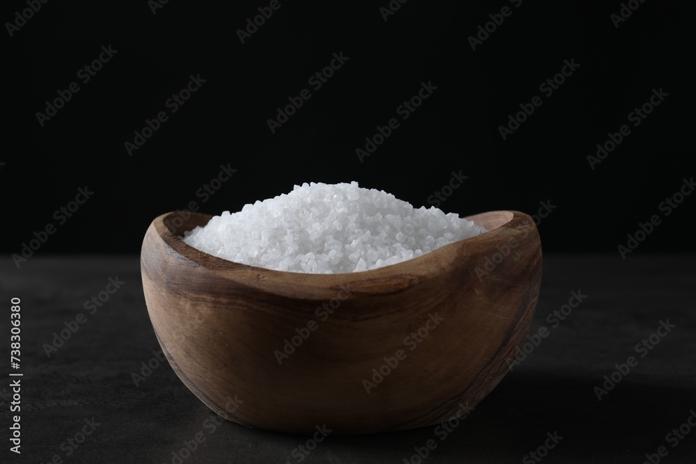 Natural salt in wooden bowl on dark grey table