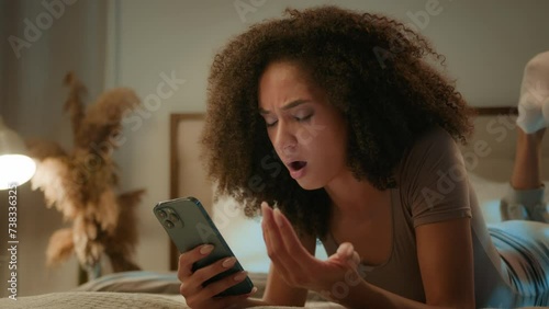 Upset shocked sad African American girl lady disappointed ethnic woman worried phone crash mobile error mistake scam message frustrated female on bed evening home with smartphone loss failure bad news photo