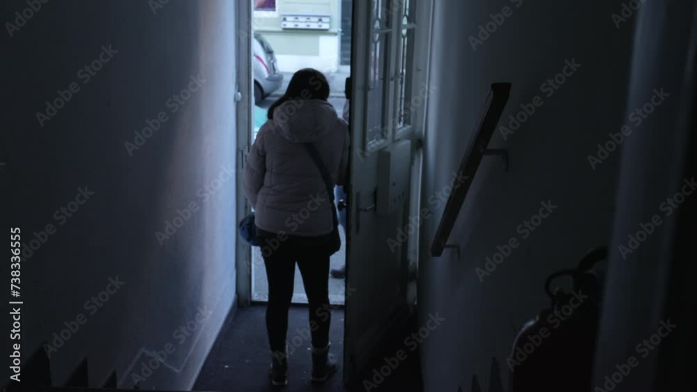 Back of woman standing by door front inside moody building entrance, chatting with someone in street ready to leave residence, blue tone Back of woman standing by door front inside moody building entrance, chatting with someone in street ready to leave residence, blue tone