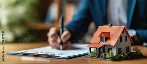 Real estate agent signing contract for client's home loan insurance with house model.