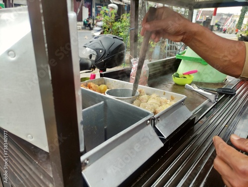 The seller preparing siomay to serve the customer. PKL or MSME concept. Siomay is Indonesian street food, consist of dumpling, steamed potato, egg and tofu with peanut sauce photo