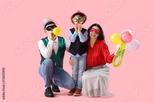 Happy family in costumes and carnival masks on pink background photo