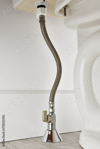 Toilet water feed line. Water valve on toilet inlet with braided hose. Ball valve vertical installation with water line coming from the floor. Toilet installation.