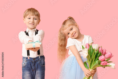 Cute little children with bouquet of beautiful tulips and gift box on pink background. International Women's Day