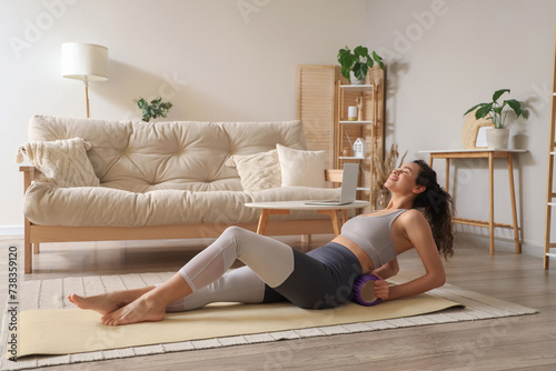 Sporty young African-American woman training with foam roller at home