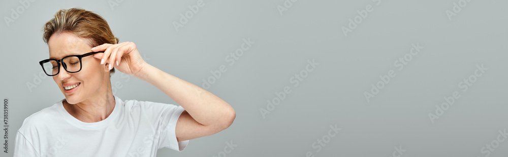 joyful appealing woman with blonde hair and glasses posing on gray backdrop and looking away, banner joyful appealing woman with blonde hair and glasses posing on gray backdrop and looking away, banner